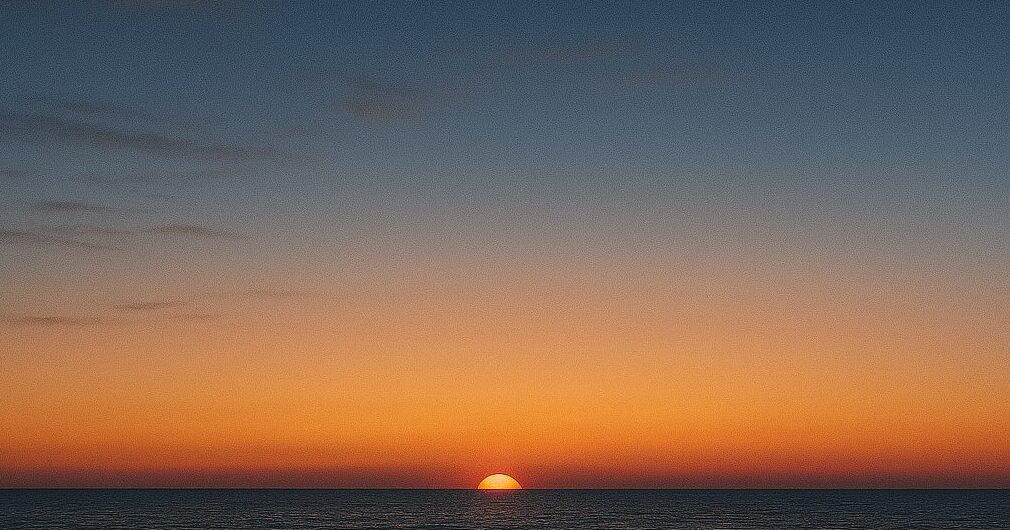 夜明け前の静かな空。深い紺色から淡い紫へと移り変わる空に、地平線の向こうからほのかな光が差し始める幻想的な風景